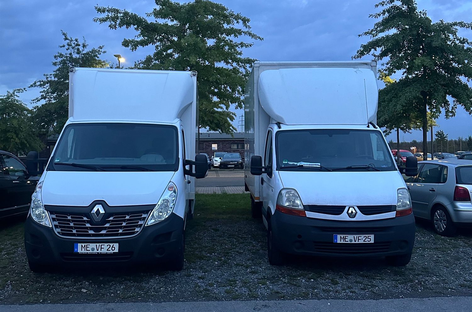 Zwei weiße Koffertransporter von Sicher Umzug stehen abends nebeneinander auf dem Hof